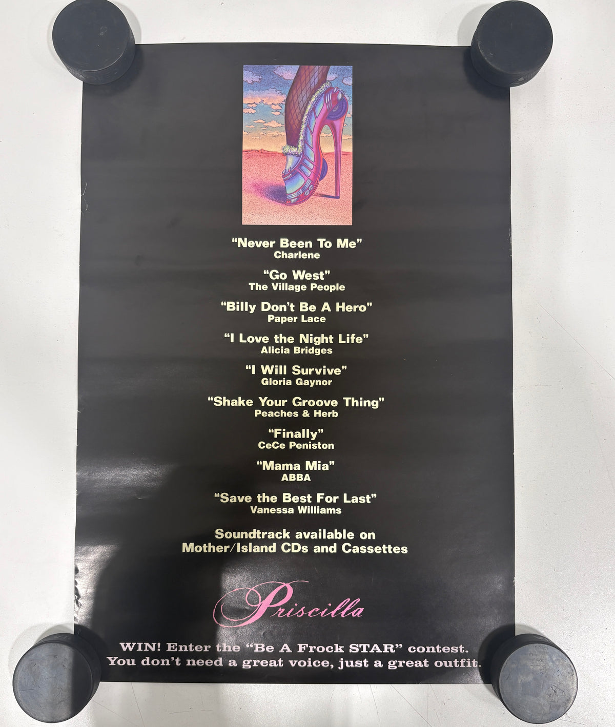 A black poster for the 1975 soundtrack album 'Be A Rock STAR' featuring a colorful illustration of a high-heeled shoe and a list of Piscilla performance songs, held down by four black weights at the corners.