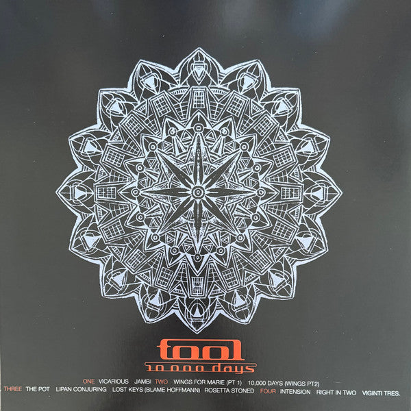A square black print or cover featuring a large white mandala-style geometric emblem centered on a dark background, with orange text reading 'tool' and smaller white text below listing track titles and tour dates.