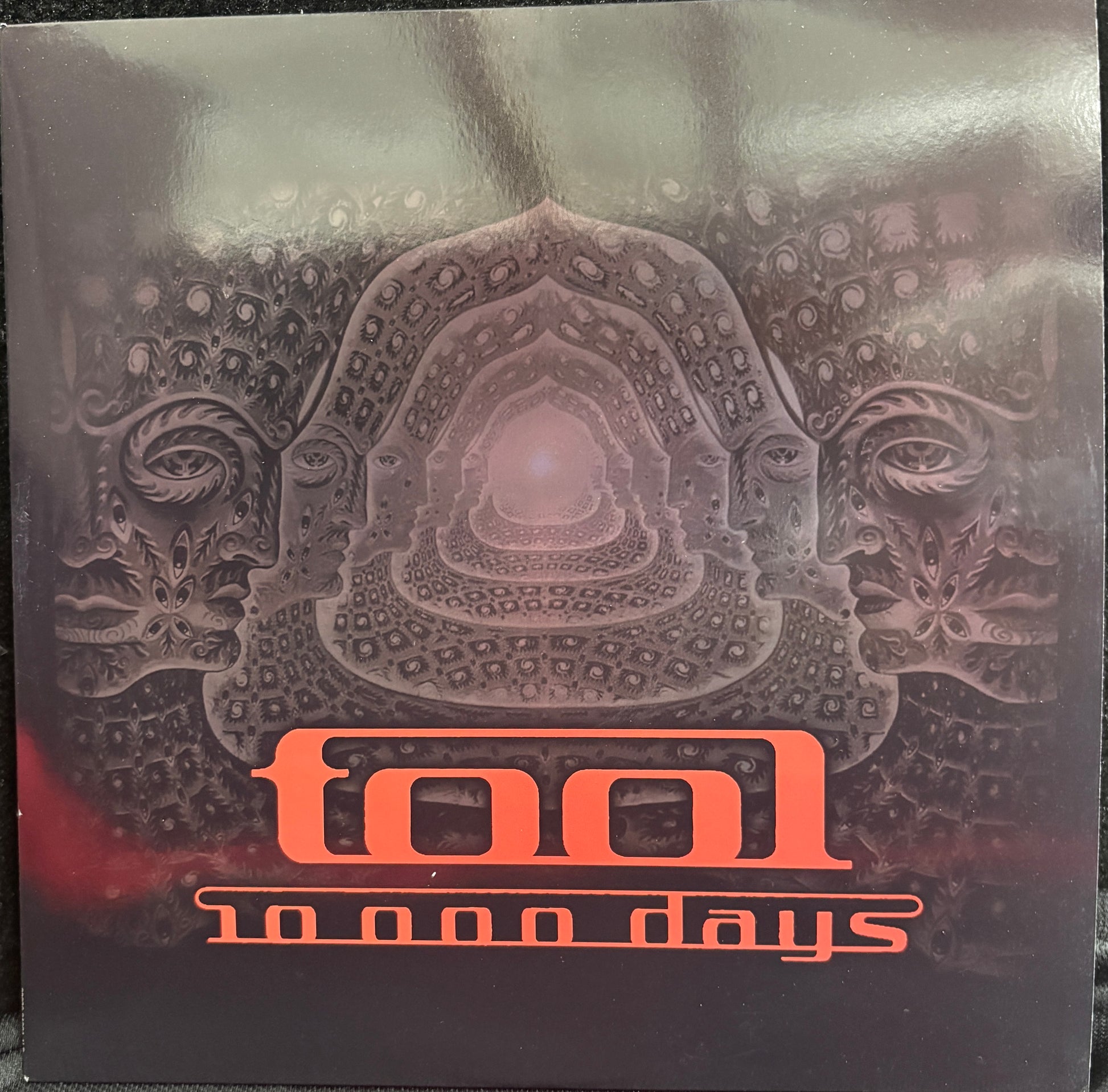 Tool's '10,000 Days' album cover, featuring a dark, intricate psychedelic illustration with the band's name in orange text at the bottom.